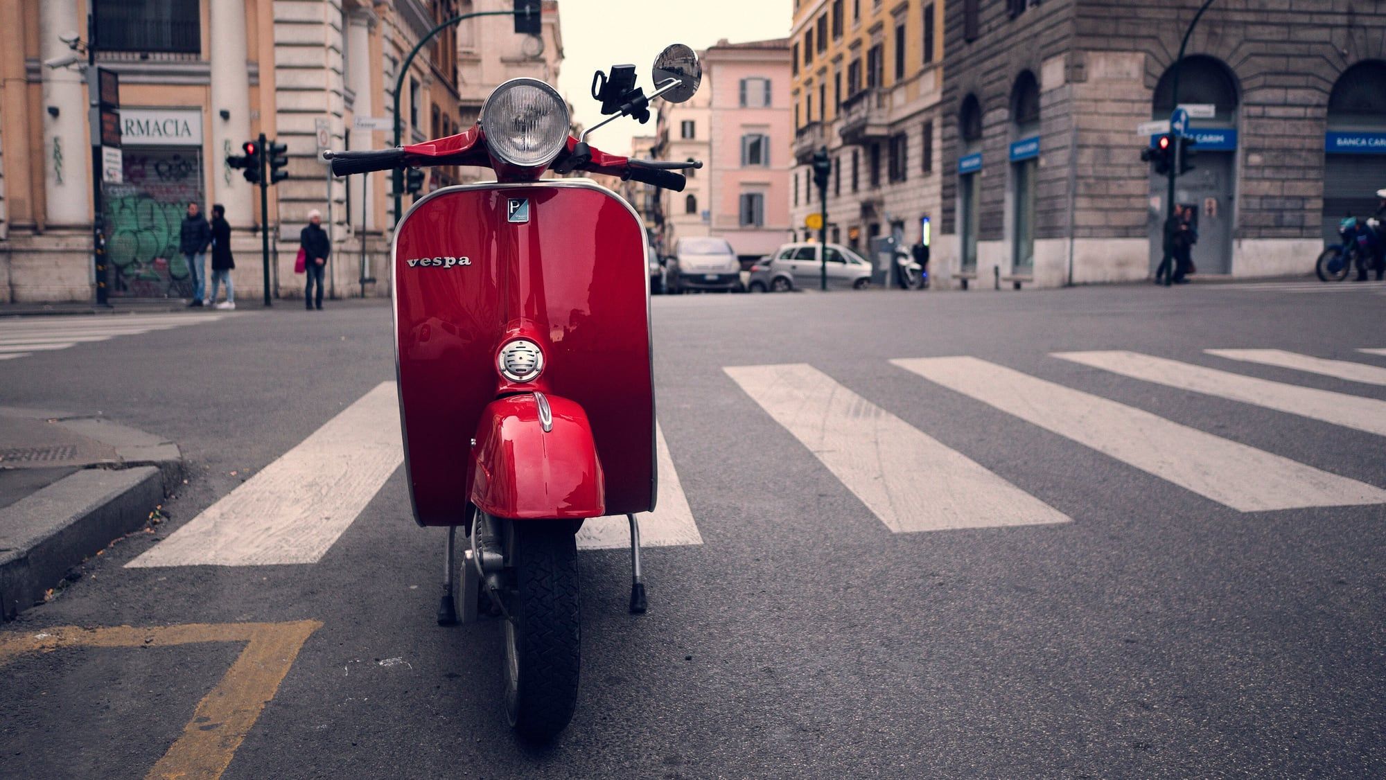 Two vintage Vespa scooters with riders in helmets on a cobbled street below the Aventine Hill in Rome
